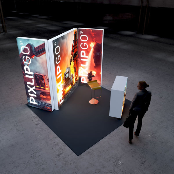 A Pixlip GO exhibition booth with a high-energy firefighting theme. The illuminated panels feature dramatic visuals of firefighters in action, flames, and firefighting equipment. The main panel showcases a firefighter with protective gear and a robotic fire suppression tool. A counter displays related imagery, and a person observes the booth.